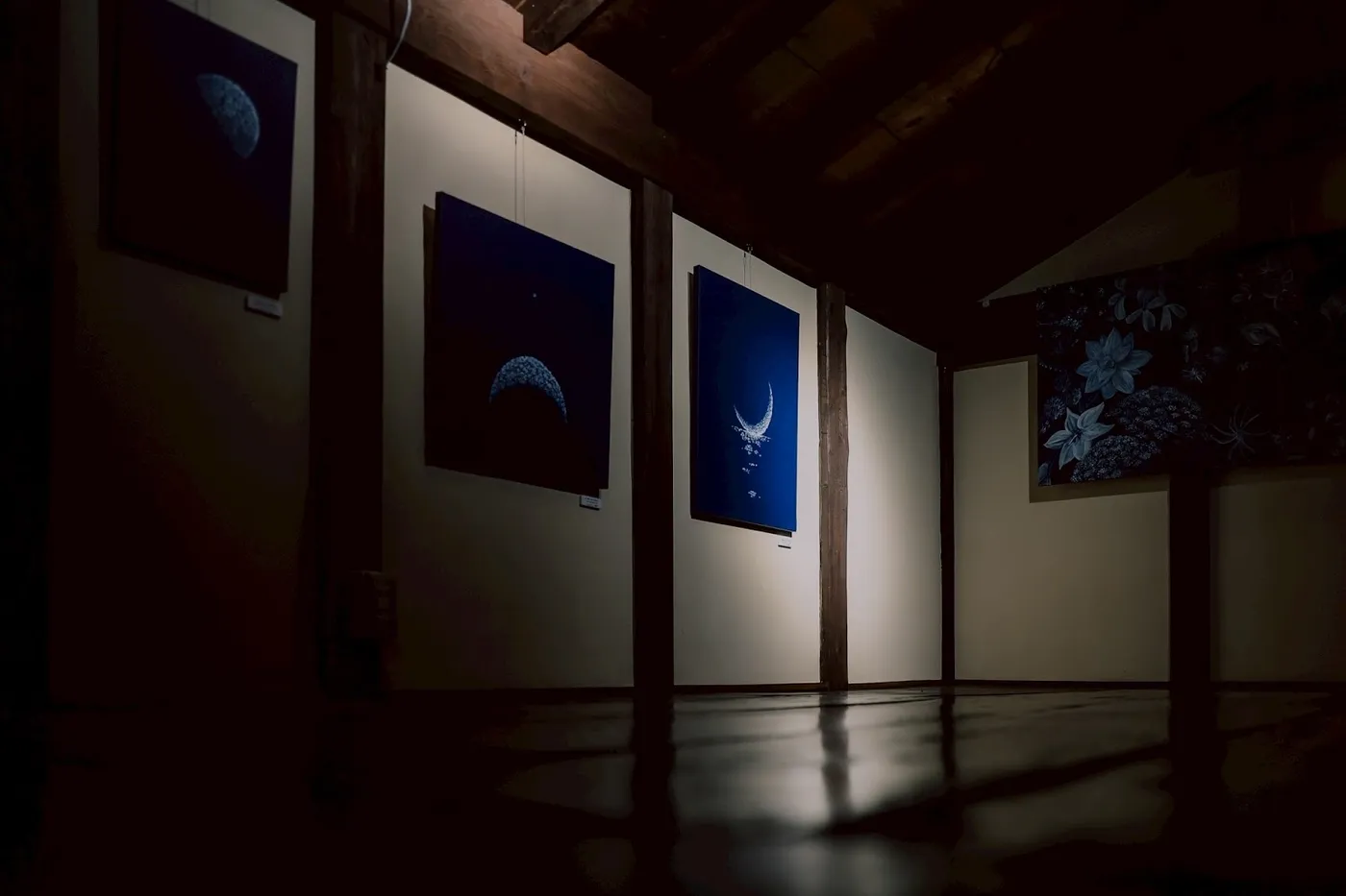 暗い室内に藍色の絵画が並ぶ展示